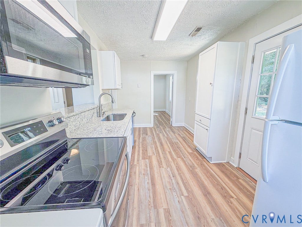 Kitchen featuring wood-finish flooring, white cabinetry, granite-style countertops, stainless steel appliances, and a built-in pantry