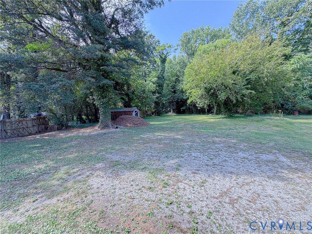 Expansive gravel and grass area with mature trees and a detached shed
