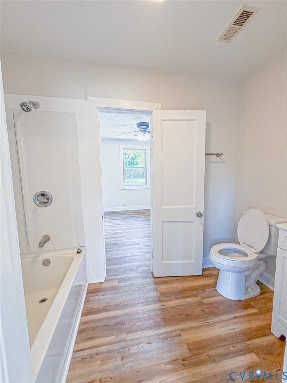 White bathtub and shower combination with chrome fixtures, wood-finish flooring, and a white toilet