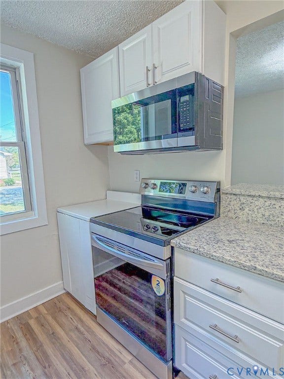 Kitchen featuring wood-finish flooring, white cabinetry with silver hardware, speckled countertops, and stainless steel appliances