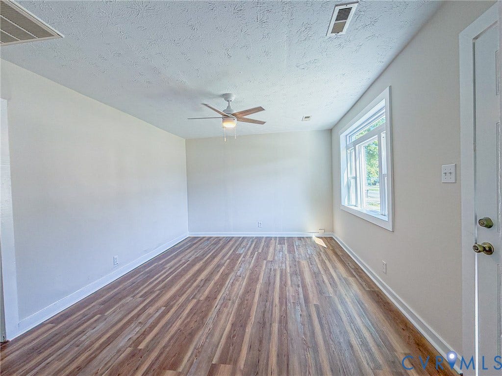 Neutral wall color, wood-finish flooring, ceiling fan with light fixture, window with white trim, white door