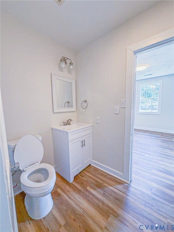 Wood-finish flooring throughout, white single vanity with cabinet storage, white framed mirror, and a two-light vanity fixture