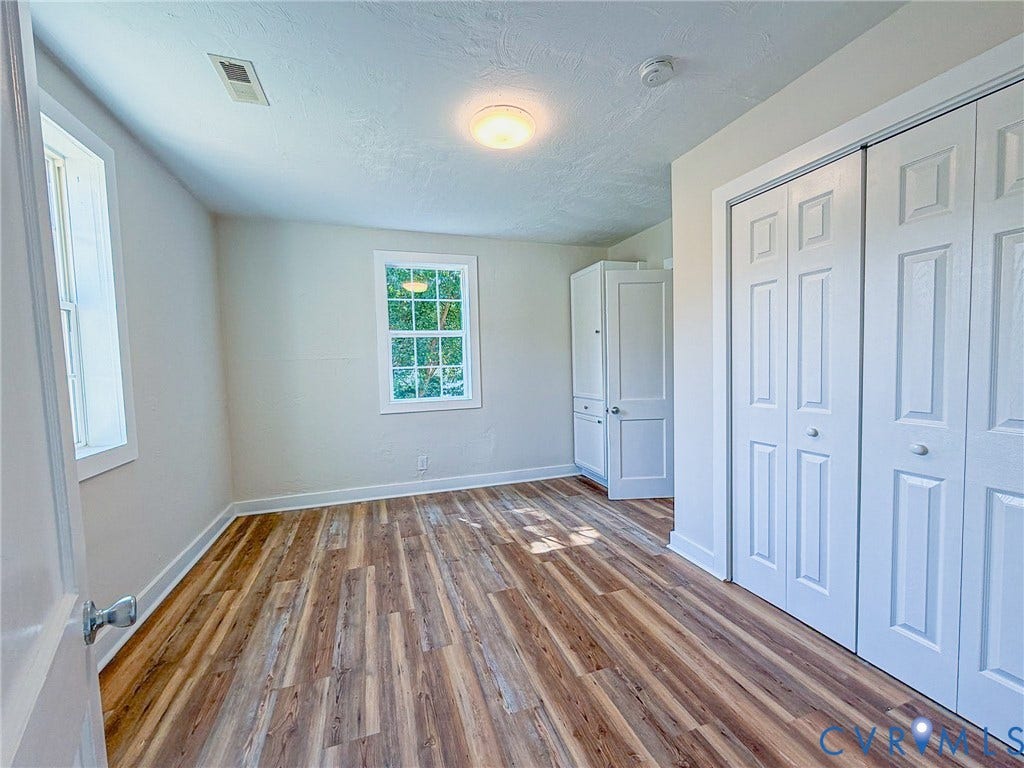 Wood-finish flooring, white bi-fold closet doors, built-in white cabinetry, window with white trim, and a ceiling-mounted light fixture