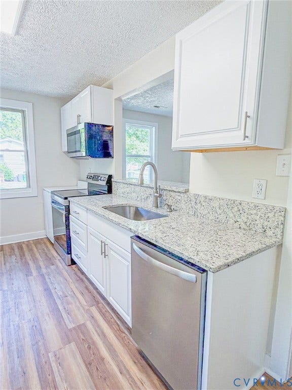 Kitchen featuring white cabinetry, stainless steel appliances, granite countertops, a stainless steel sink, and wood-finish flooring