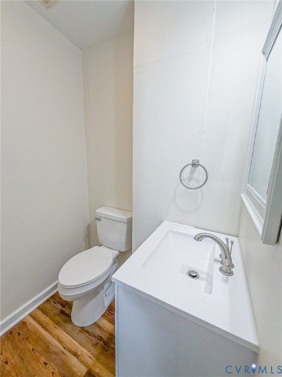 White vanity with an integrated rectangular sink and brushed nickel faucet, wood-finish flooring, and a wall-mounted toilet
