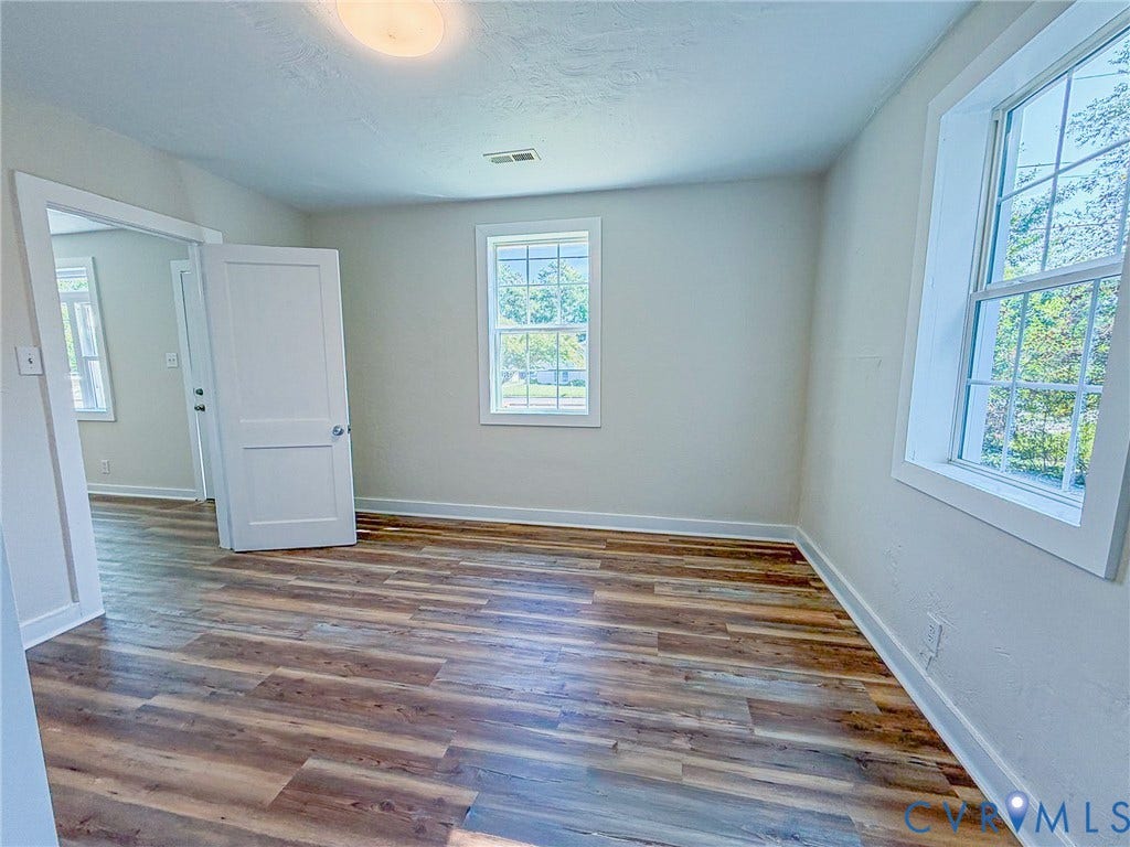 Bright room featuring wood-finish flooring, white walls, and multiple windows