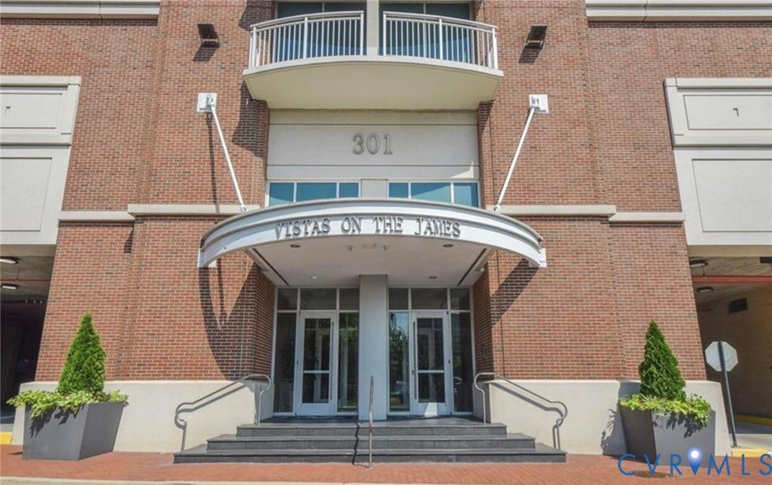 301 Virginia Street, #U703, Richmond, VA 23219 Brick facade with concrete accents, dual glass entry doors, curved entrance canopy, and second-story balcony with metal railing