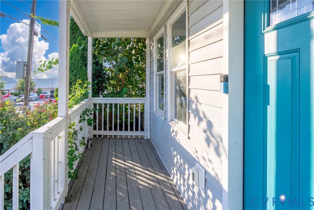 Covered front porch with wood-finish flooring, white railing, and a vibrant blue entry door
