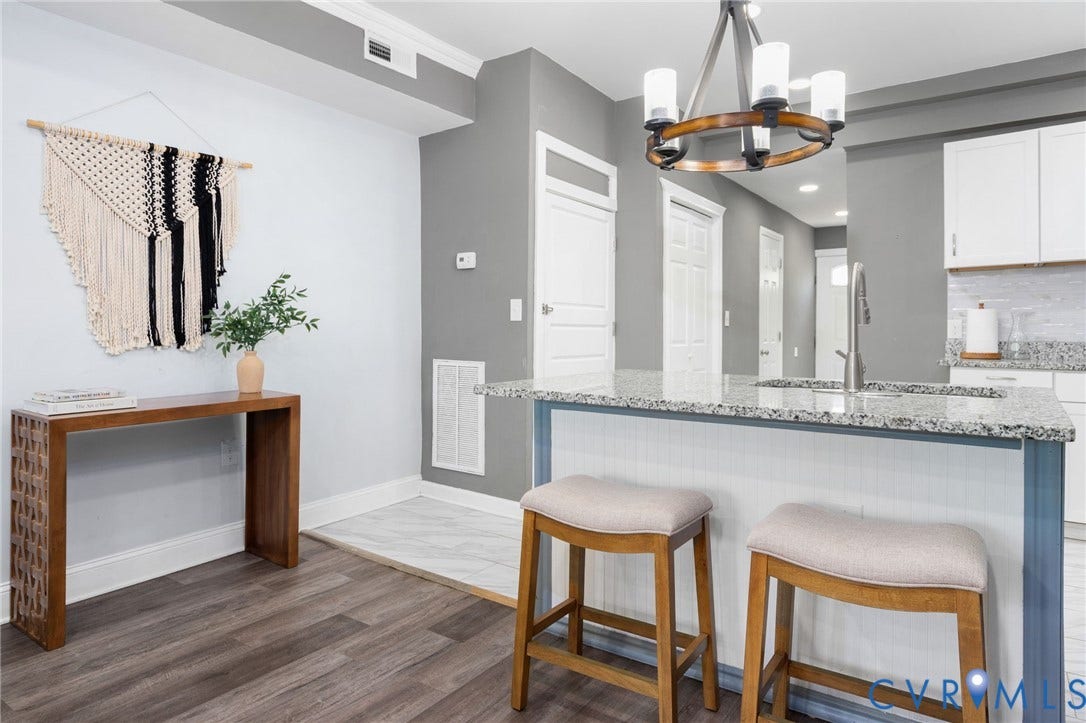 Wood-finish flooring, white trim, and a kitchen island with a stone countertop and integrated sink