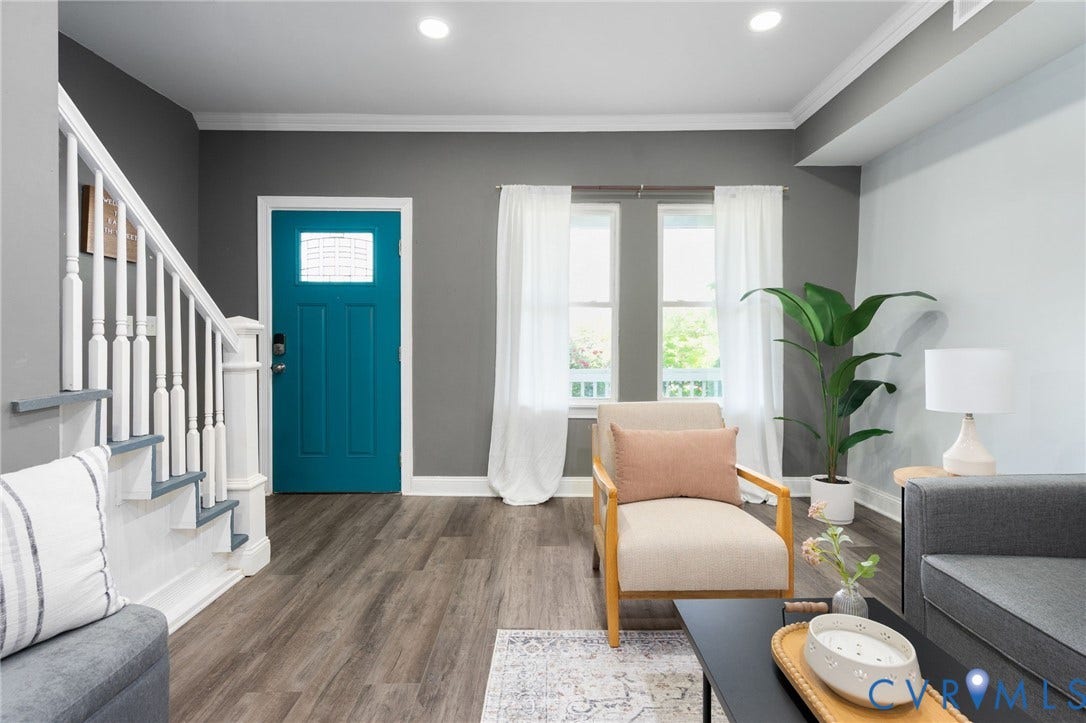 Wood-finish flooring throughout the living space, a bright teal entry door with frosted glass, white crown molding, and two multi-pane windows providing natural light