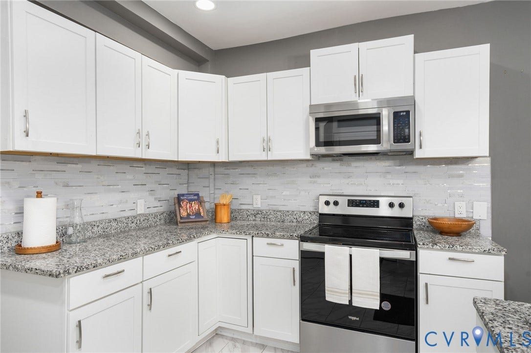 White shaker-style cabinetry with brushed nickel hardware, granite-style countertops, stainless steel microwave, and a white linear tile backsplash