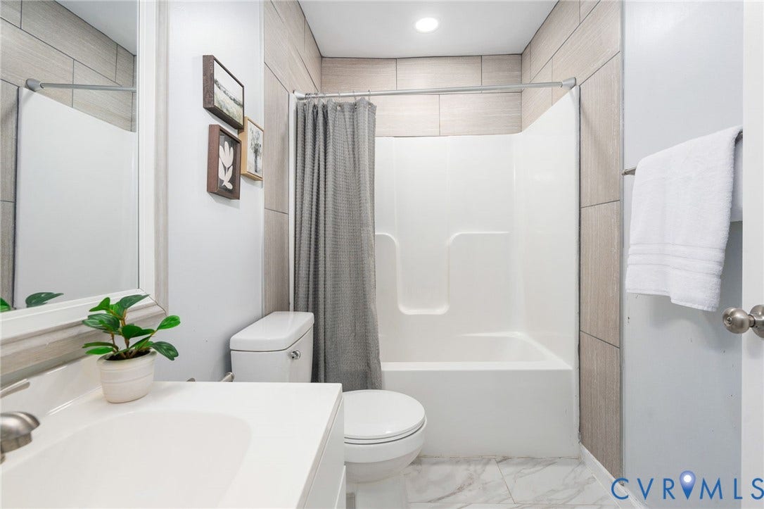 Full bathroom featuring a single vanity, a toilet, a tub-shower combination, and tiled walls with marble-look flooring