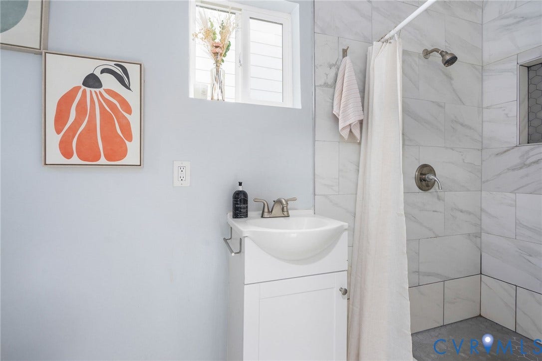 White vanity with an integrated vessel sink, brushed nickel faucet, and a shower with white veined tile