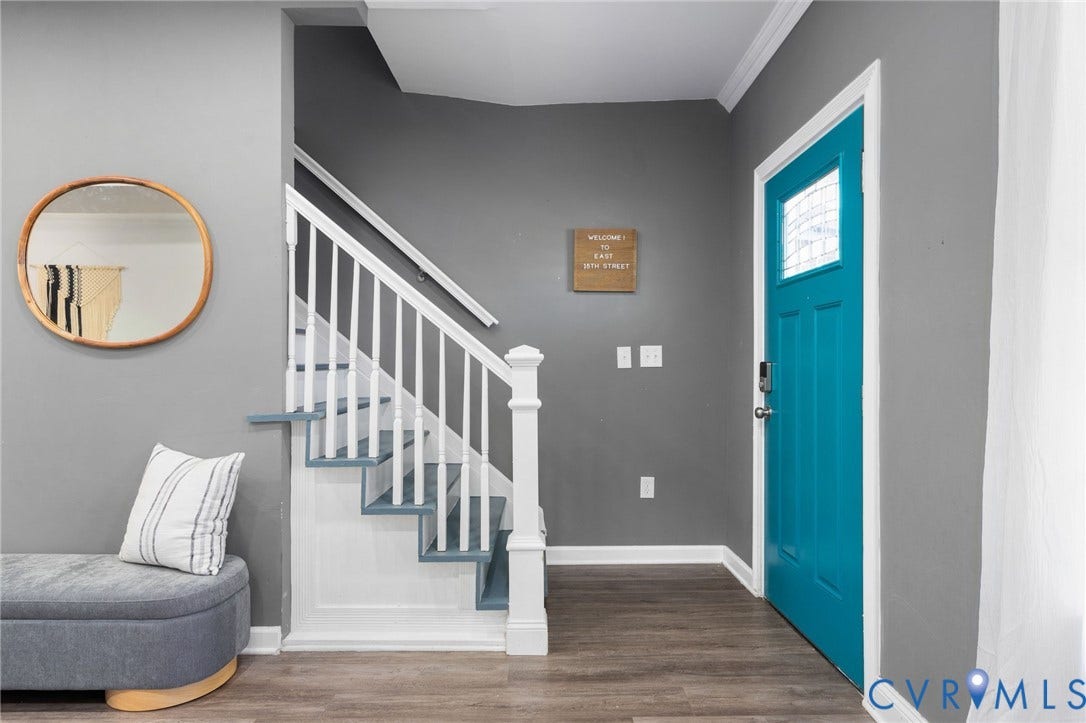 Wood-finish flooring, staircase with white newel post and balusters, and a vibrant teal entry door with decorative glass insert
