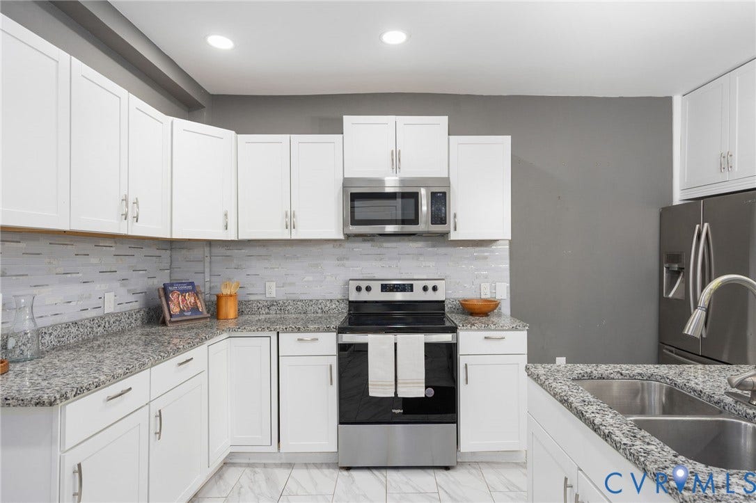 White shaker-style cabinetry with chrome hardware, speckled countertops, tile backsplash, stainless steel appliances, and dual basin sink