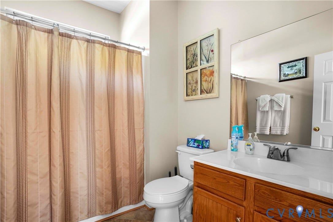 307 Poplar Dr, Louisa, VA 23093 Wood-finish vanity with an integrated sink and chrome faucet, large wall-mounted mirror, and a white toilet
