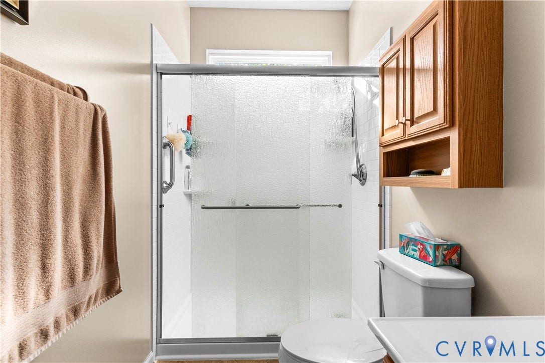 307 Poplar Dr, Louisa, VA 23093 Enclosed shower with sliding glass doors, built-in shelving, and a mounted wooden cabinet