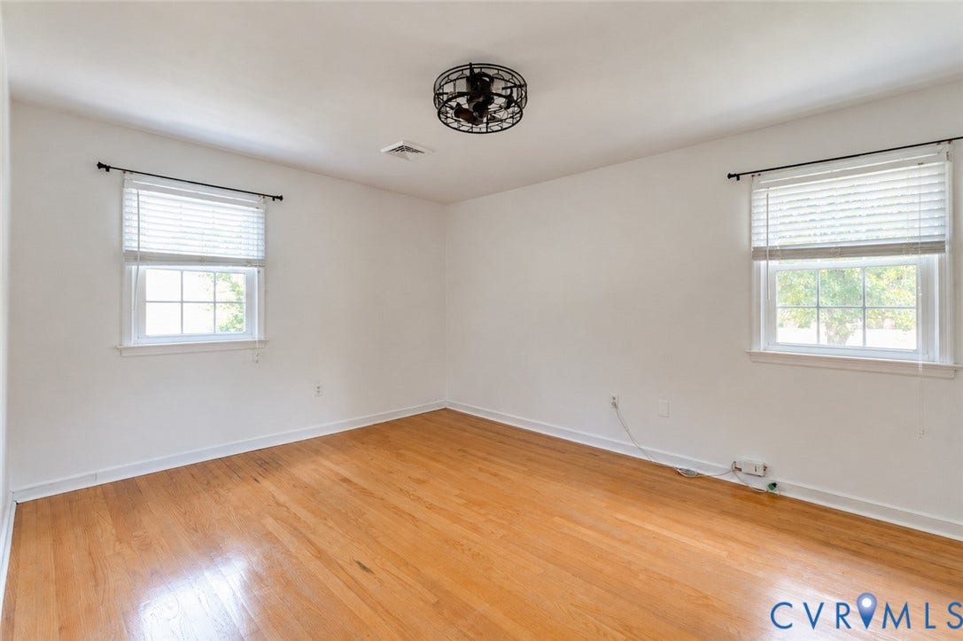 Hardwood flooring with a glossy finish, two white framed windows, and a black ornamental ceiling fan