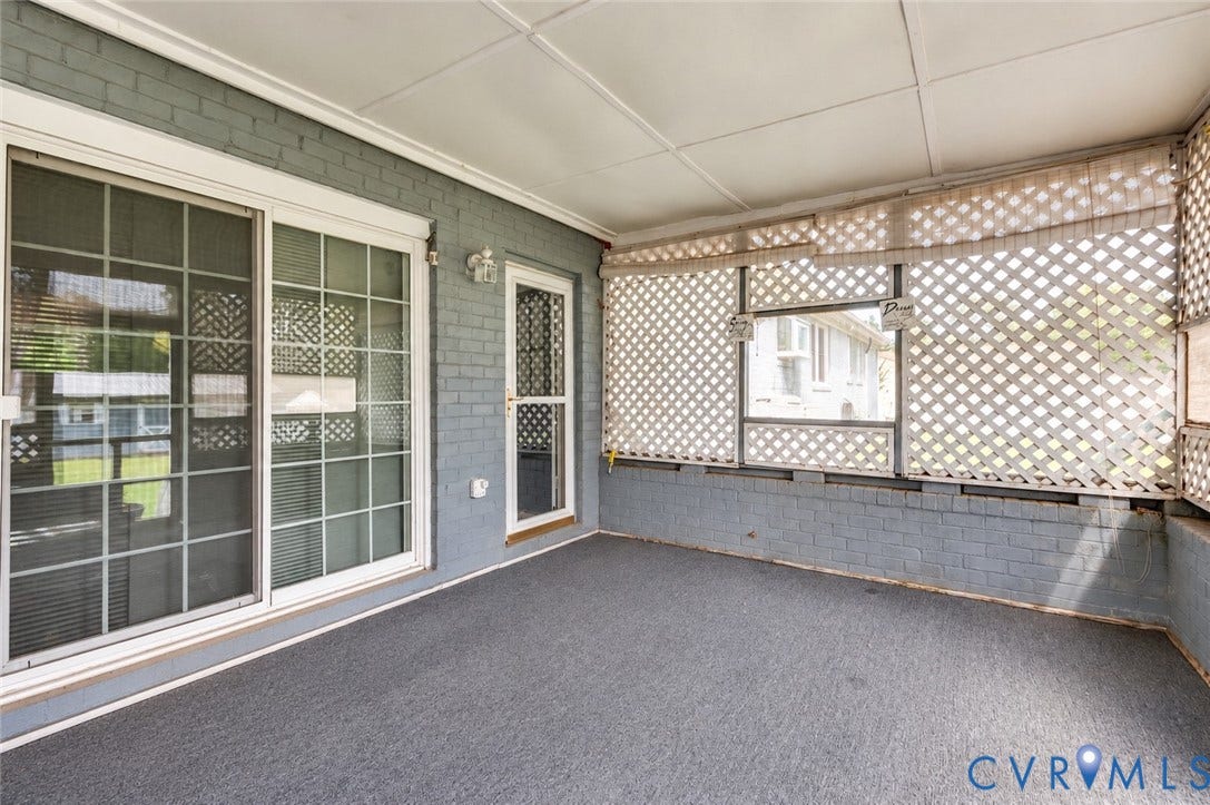 Screened porch featuring gray brick walls, sliding glass doors, a white lattice screen, and a gray carpeted floor