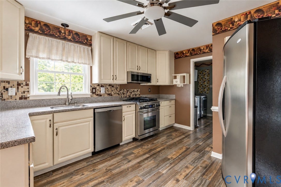 Kitchen featuring cream-colored cabinetry, stainless steel appliances, wood-finish flooring, and a mosaic tile backsplash