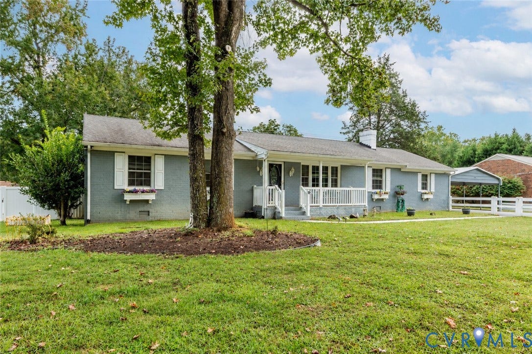 Gray exterior with white shutters and window boxes, covered front porch with white railing, and a detached carport