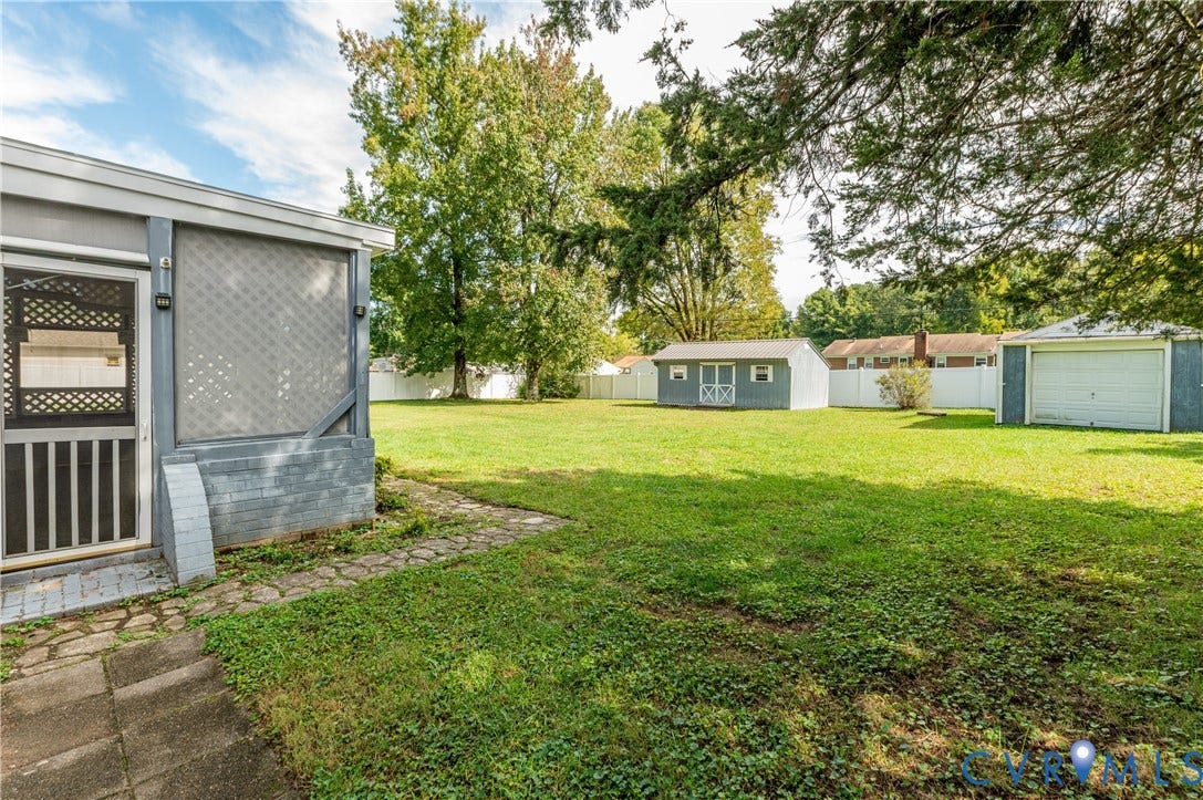 Expansive grassy lawn with a stone pathway, a screened porch, a detached storage shed, and a detached garage
