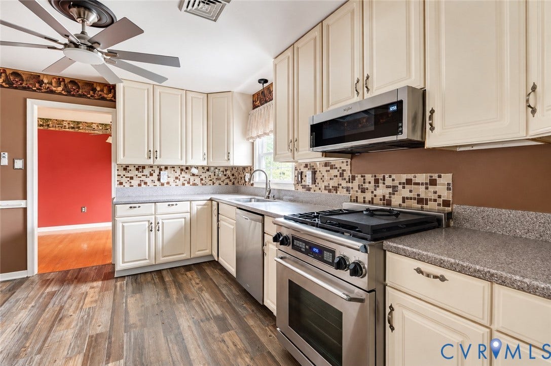 Kitchen featuring wood-finish flooring, cream cabinetry, stainless steel appliances, mosaic tile backsplash, and a ceiling fan