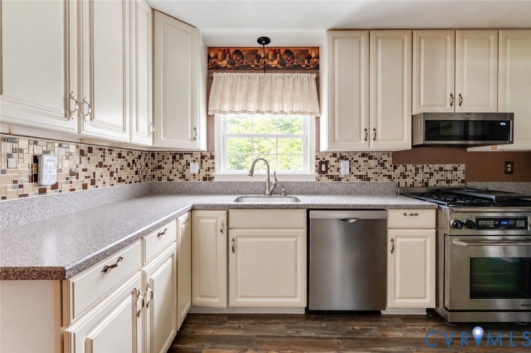 Cream-colored cabinetry with decorative hardware, mosaic tile backsplash, stainless steel appliances, and a stainless steel sink with a gooseneck faucet