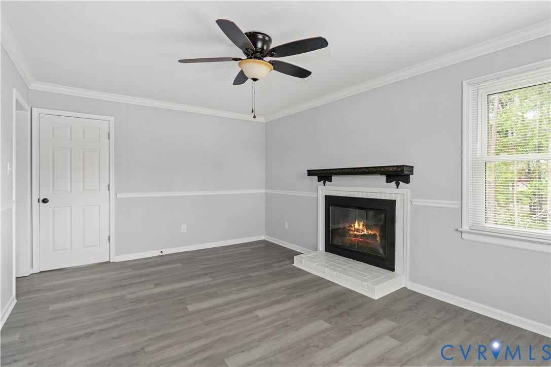 5221 Ecoff Avenue, Chester, VA 23831 Wood-finish flooring, ceiling fan with light fixture, fireplace with black mantel and white brick surround, and paneled interior door