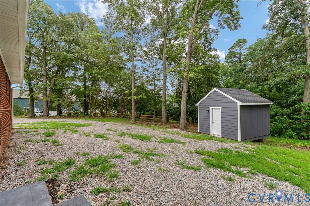 5221 Ecoff Avenue, Chester, VA 23831 Expansive gravel yard featuring a newly constructed shed with siding and a shingled roof, surrounded by mature trees