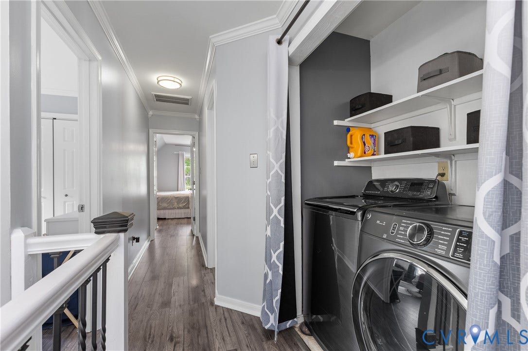 7625 Southford Lane, Chesterfield, VA 23832 Dedicated laundry room featuring front-load washer and dryer with stacked configuration, open shelving with integrated storage, dark accent wall, wood-finish flooring, and bright overhead lighting throughout the hallway corridor