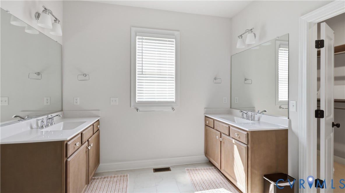 Dual vanity with integrated sinks, wood-finish cabinetry, and wall-mounted lighting