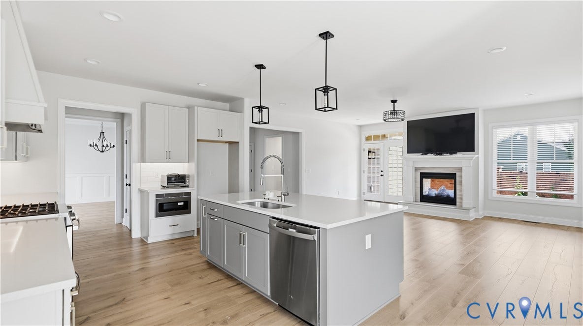 Open-concept living space featuring a central kitchen island with a white countertop, light wood-finish flooring, a built-in fireplace, and a glass-paned door