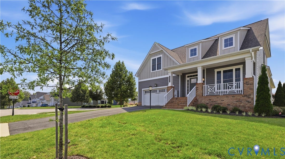 Two-story residence featuring a brick and siding exterior, front porch with white railing, dormer windows, and an attached two-car garage