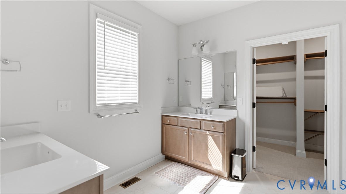 Dual vanity with integrated sinks, wood-finish cabinetry, wall-mounted lighting, and a walk-in closet with built-in shelving