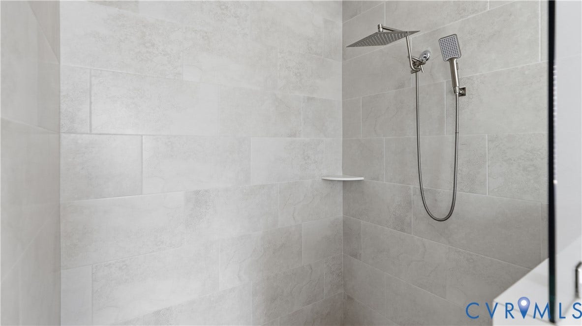Tiled shower enclosure with a rain showerhead, handheld shower, and an integrated corner shelf
