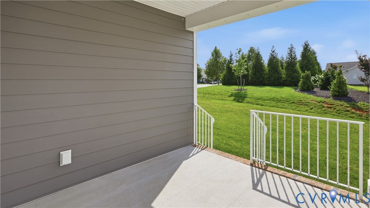 Covered patio with concrete flooring and white railings, opening to a spacious lawn with mature plantings