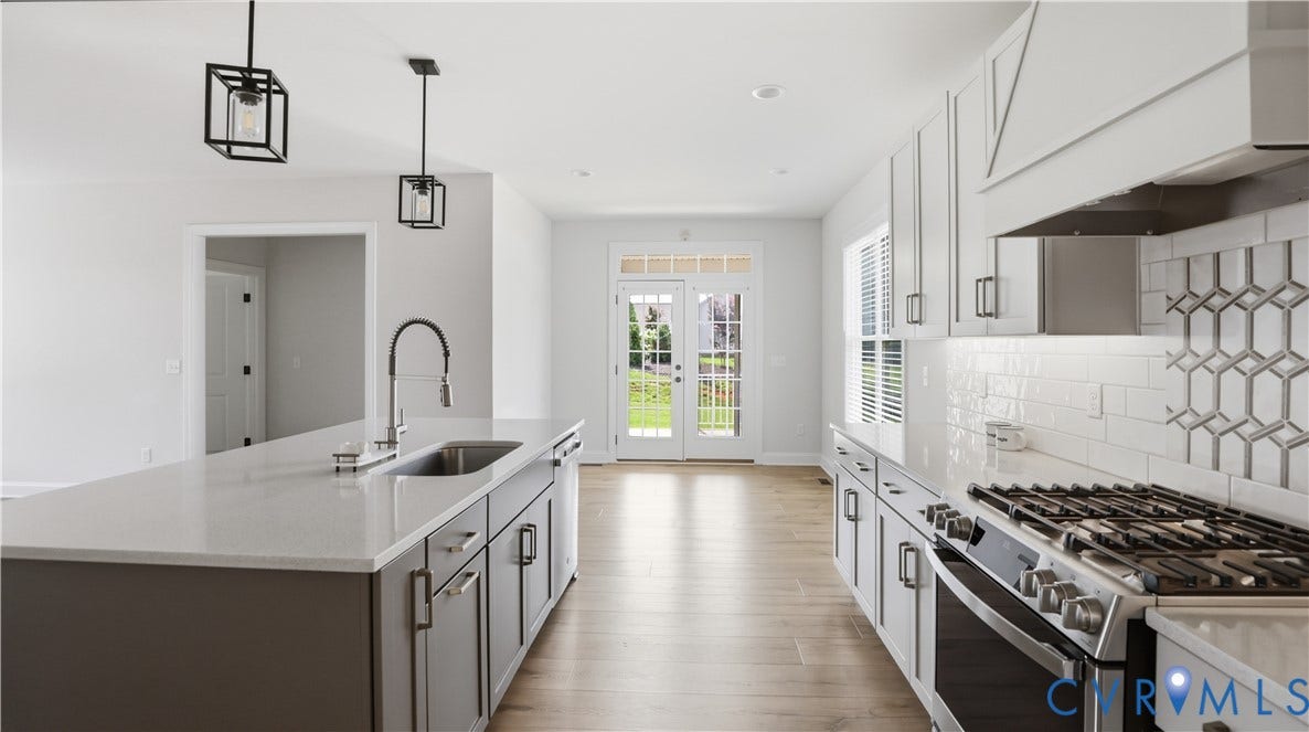 Modern kitchen featuring an island with an undermount sink, pendant lighting, stainless steel appliances, and wood-finish flooring