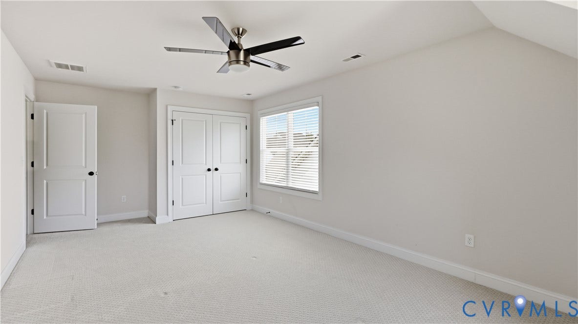 Wall-to-wall carpeting, window with blinds, ceiling fan with light fixture, and two panel doors