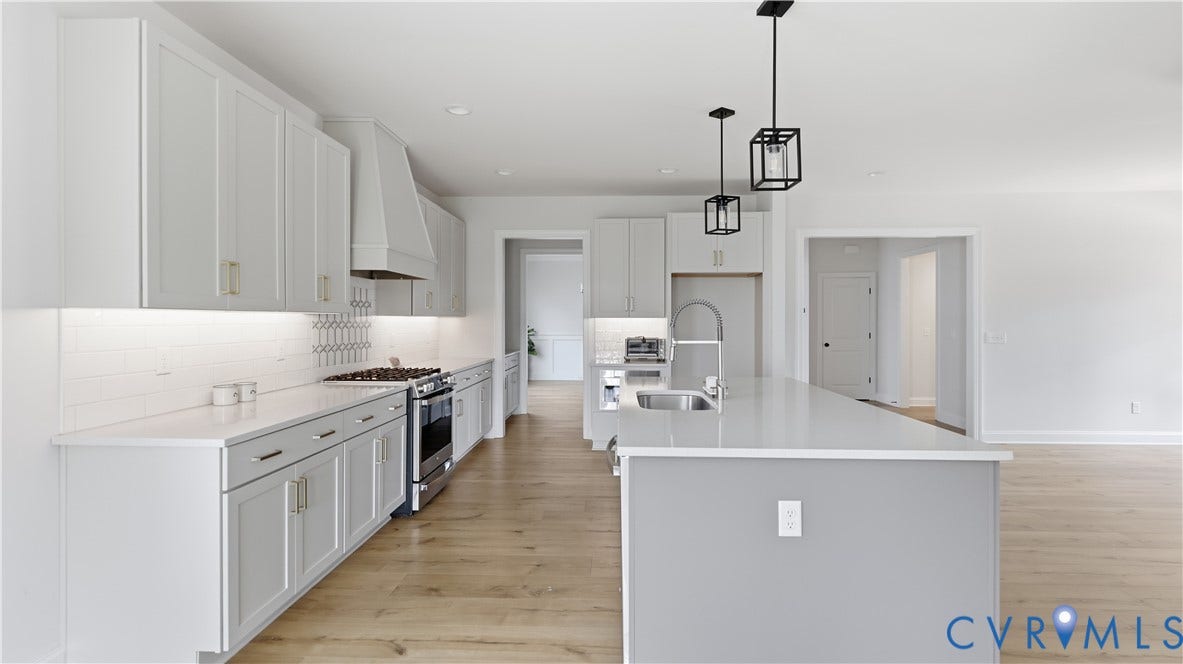 Modern kitchen featuring light cabinetry, stainless steel appliances, a large island with sink, pendant lighting, and wood-finish flooring
