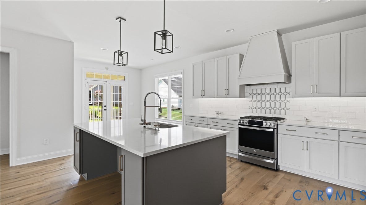 Kitchen featuring an island with a built-in sink, stainless steel range, white subway tile backsplash, decorative tile accent, and light wood-finish flooring
