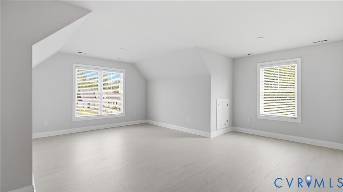 Expansive room featuring light wood-finish flooring, multiple windows with blinds, and clean, neutral wall tones