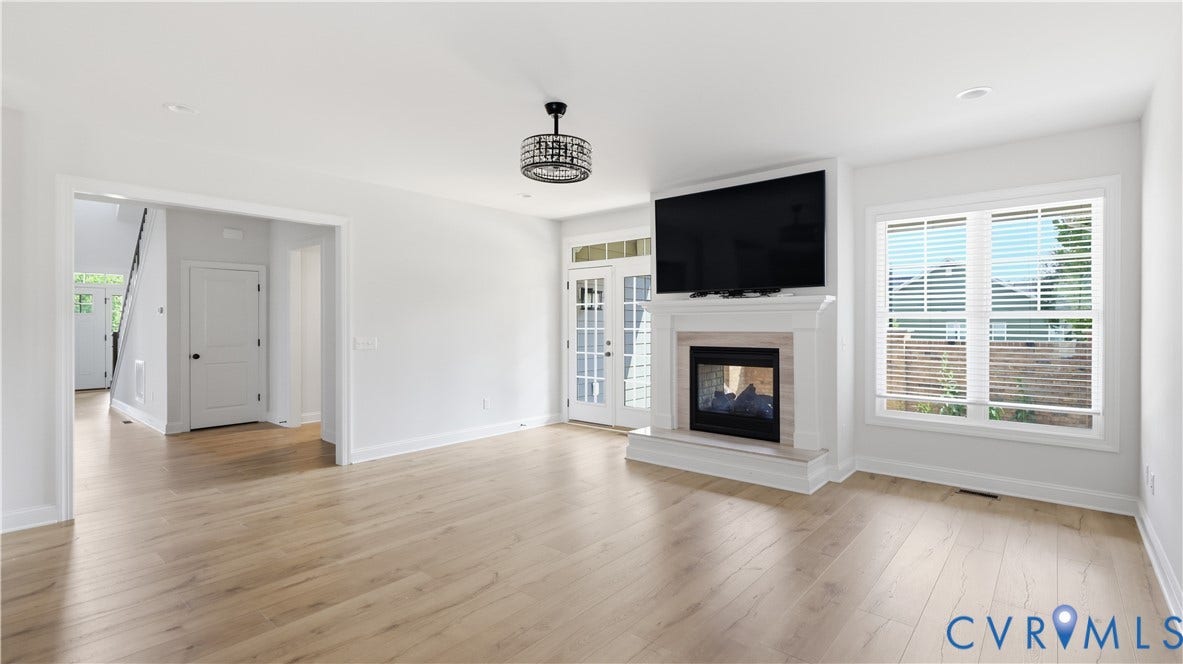 Recessed lighting, wood-finish flooring, a contemporary chandelier, and a white fireplace with a stone surround