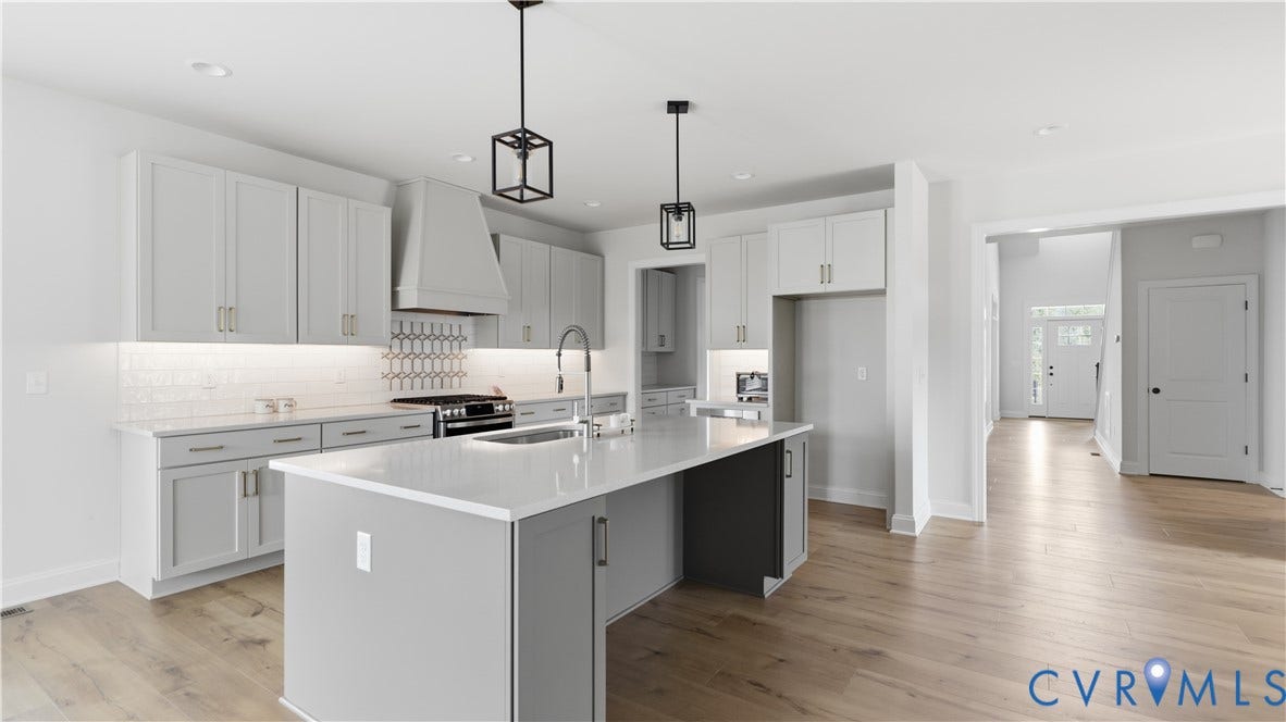 Spacious kitchen featuring an island with a quartz countertop, light wood-finish flooring, light gray cabinetry, and geometric tile backsplash