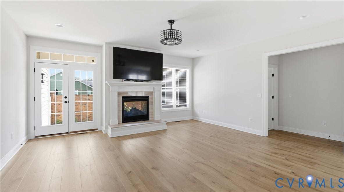 Wood-finish flooring throughout, featuring a fireplace with a white mantel, and a built-in television mount