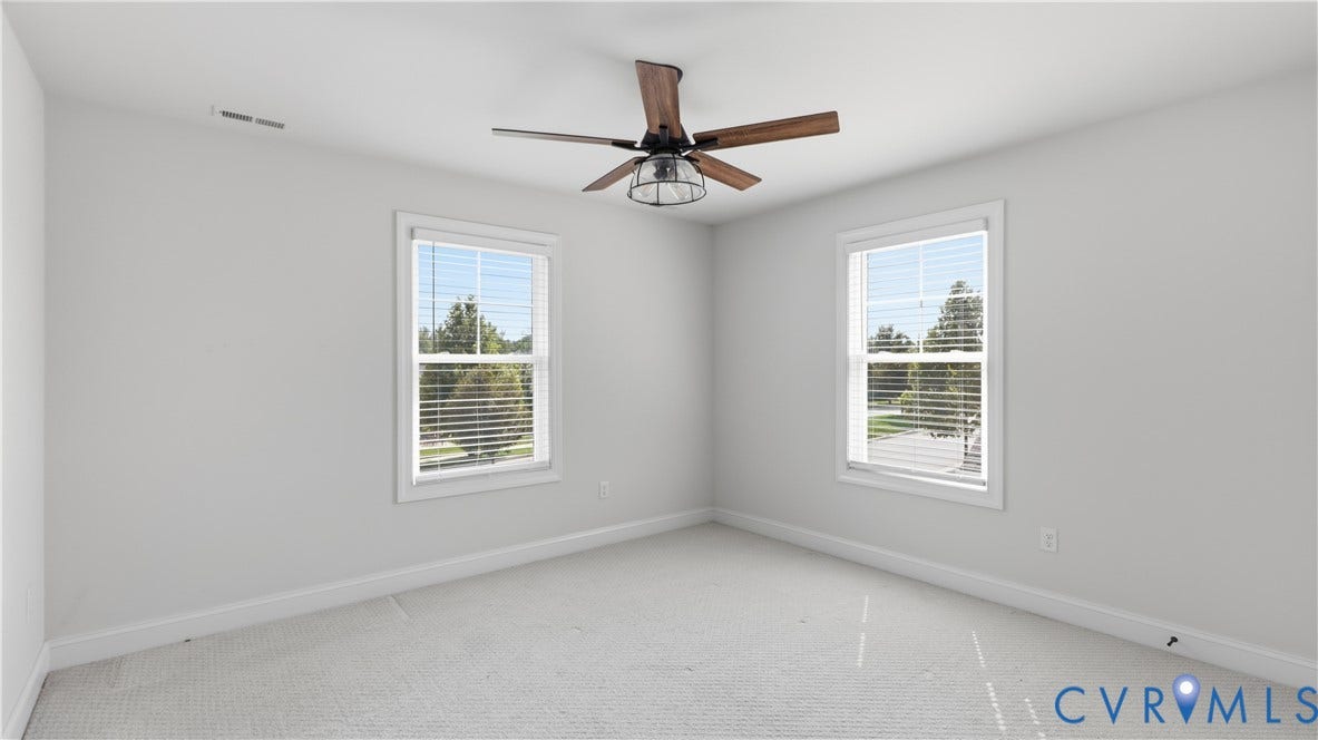 Bright room featuring two windows with horizontal blinds, a ceiling fan with wood-finish blades, and neutral-toned carpeting