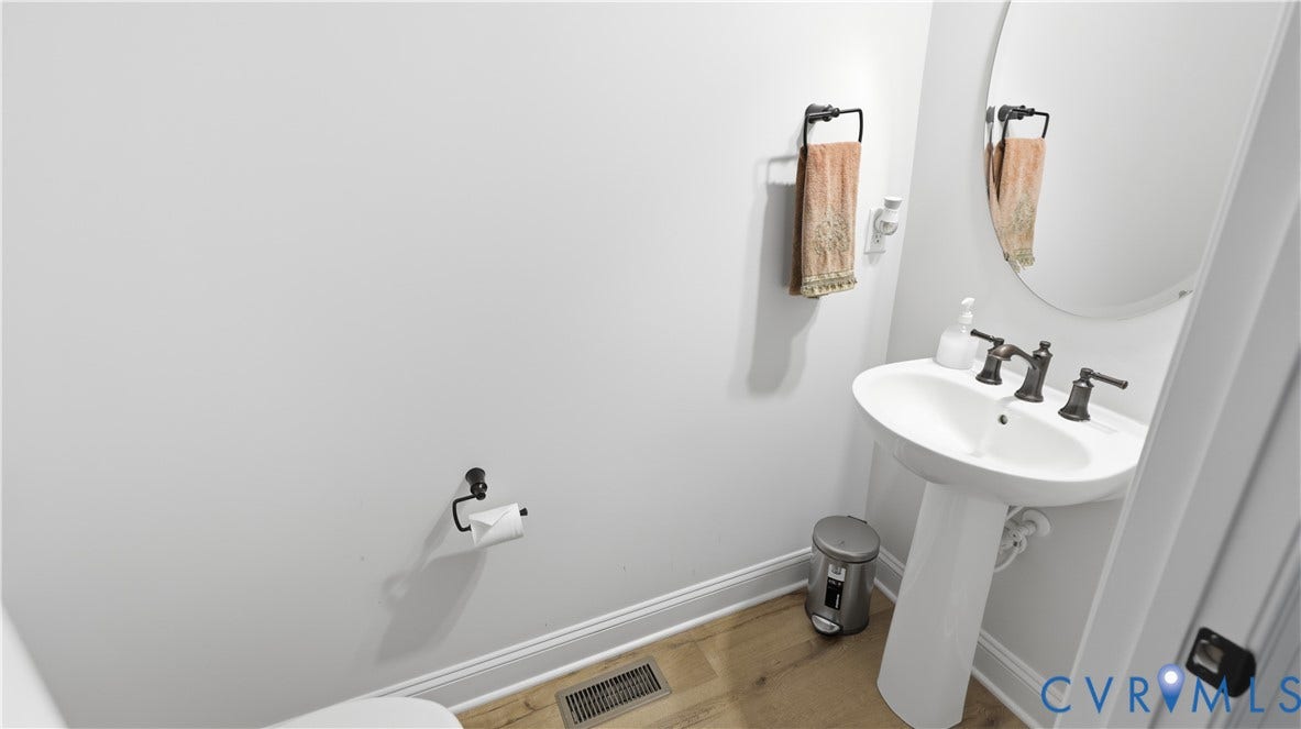 Pedestal sink with dark-toned fixtures, oval mirror, and light-toned wood-finish flooring