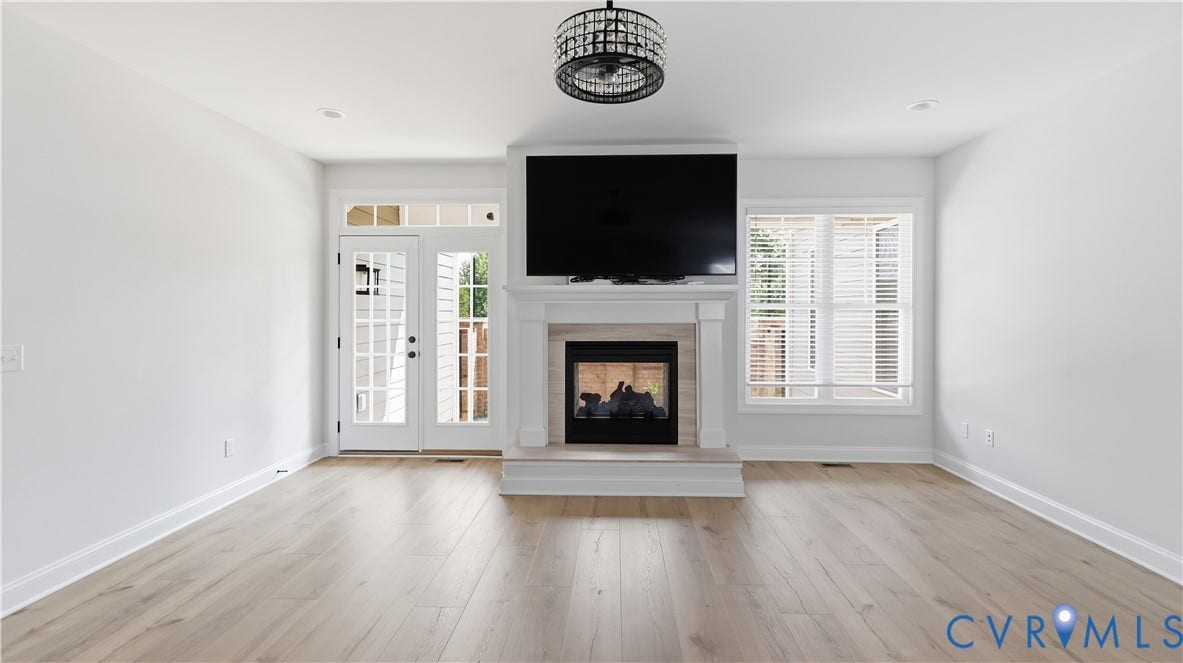 Recessed lighting, wood-finish flooring, white walls, double glass-paneled doors, and a decorative fireplace with a mantel