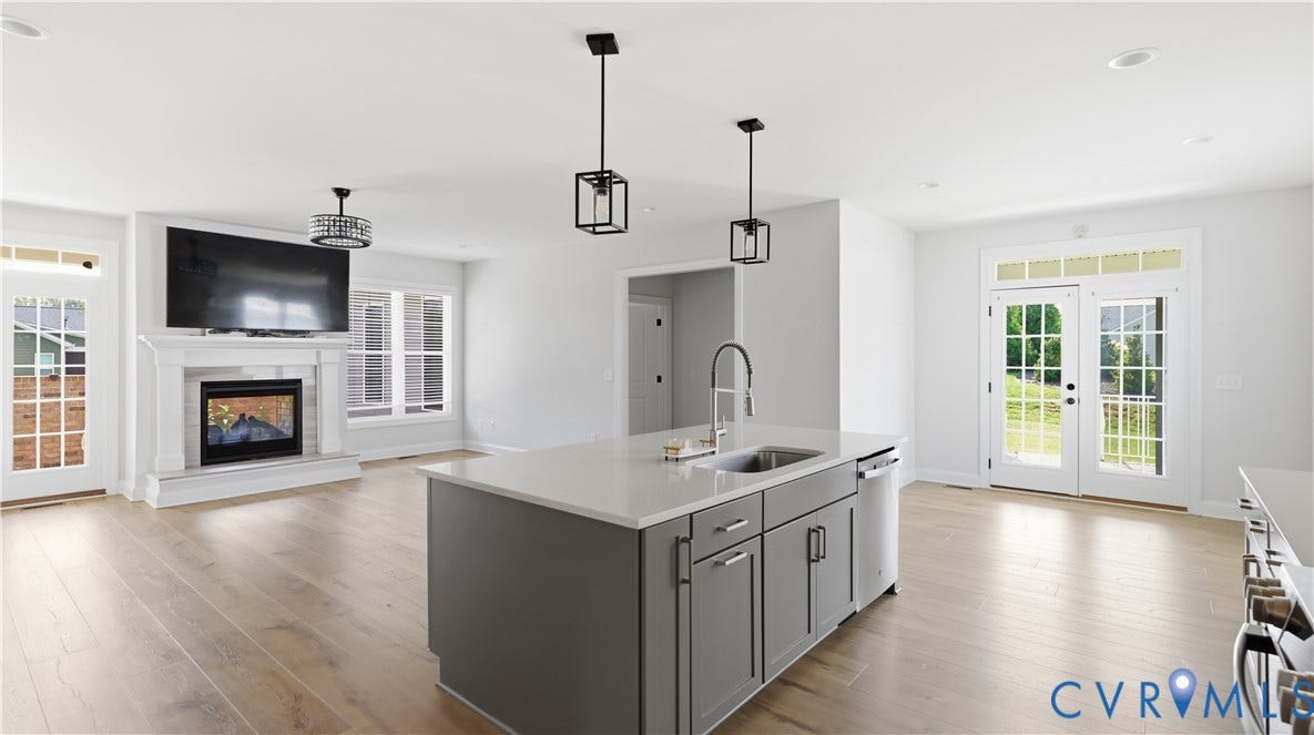 Engineered wood flooring, built-in fireplace, kitchen island with sink, pendant lighting, and French doors