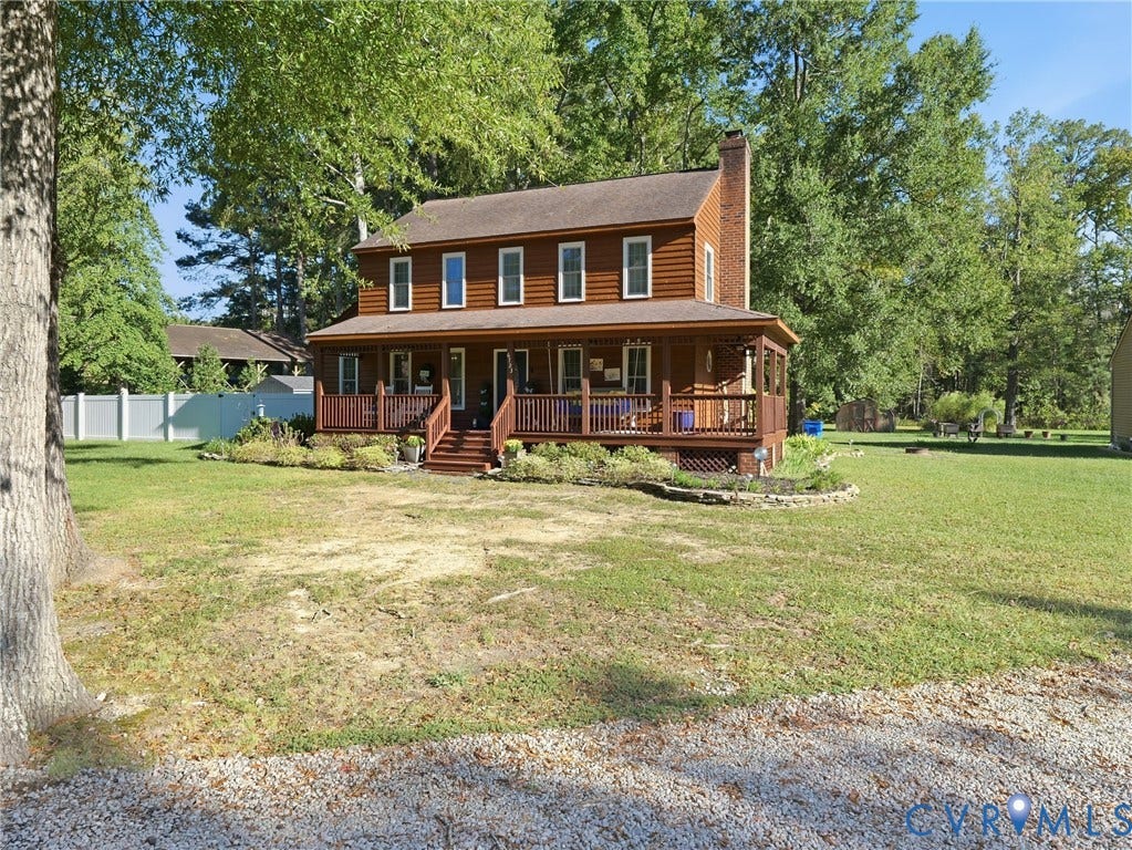 6723 Bull Hill Road, Prince George, VA 23875 Two-story log cabin exterior featuring a wraparound covered porch, exterior brick chimney, stone-lined landscaping beds, and expansive yard
